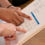 Dwie osoby analizują szczegóły faktury, wskazując dane na wydruku