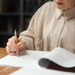 Kobieta przy biurku sprawdzająca wydruki i robiąca notatki