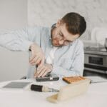 Mężczyzna w okularach naprawia sprzęt AGD śrubokrętem przy stole kuchennym
