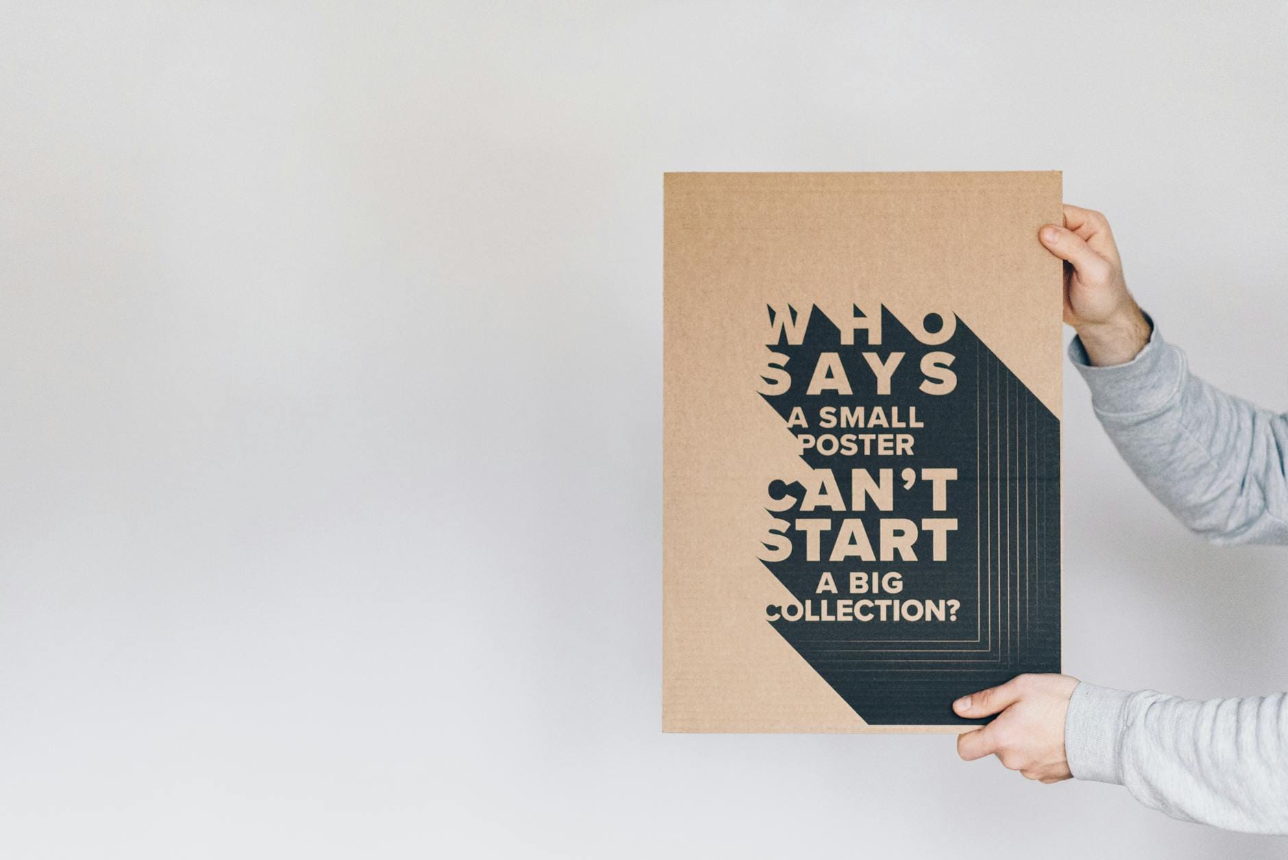 Mężczyzna trzyma biały prostokątny plakat z tytułem i znakiem zapytania