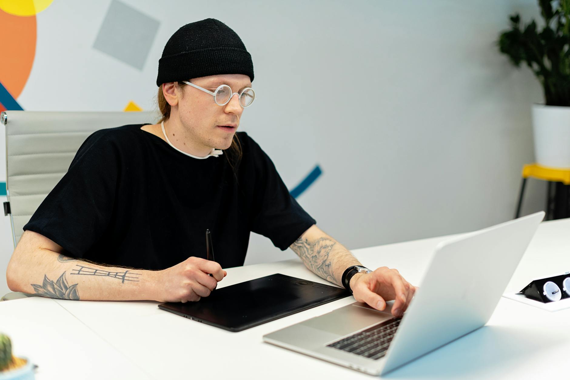 Wytatuowany projektant pracuje na laptopie i tablecie w biurze