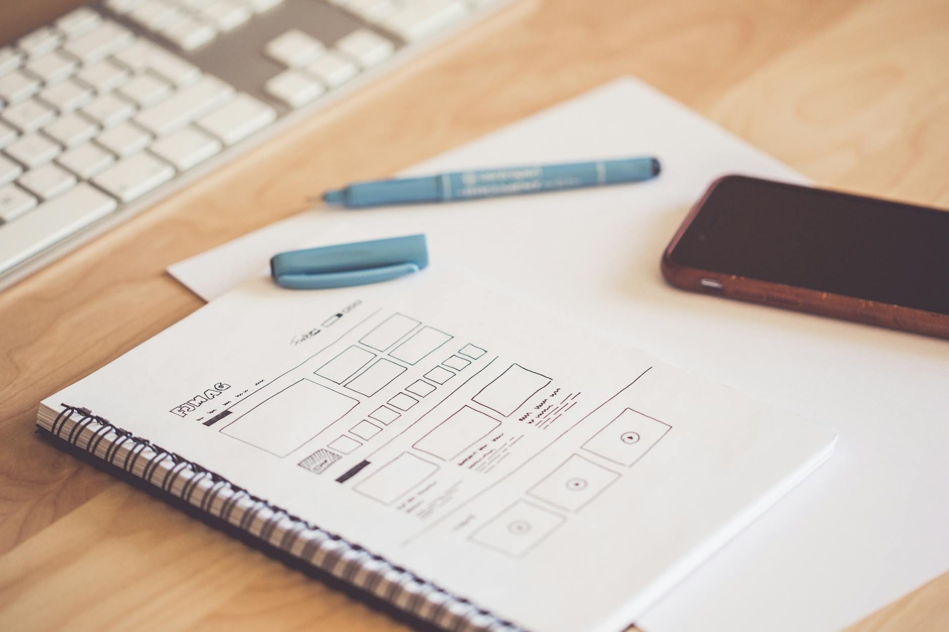 Biurko z szkicami wireframe, smartfonem i klawiaturą na drewnianym blacie