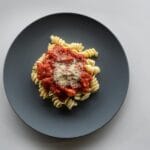 Makaron fusilli z sosem pomidorowym i parmezanem na ciemnym talerzu