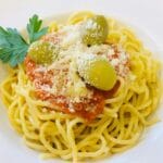 Spaghetti z sosem pomidorowym, oliwkami i tartym serem na białym talerzu