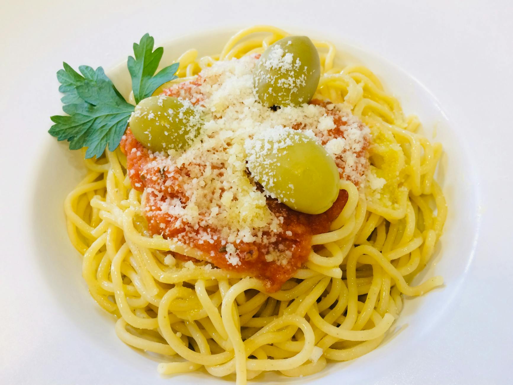 Spaghetti z sosem pomidorowym, oliwkami i tartym serem na białym talerzu